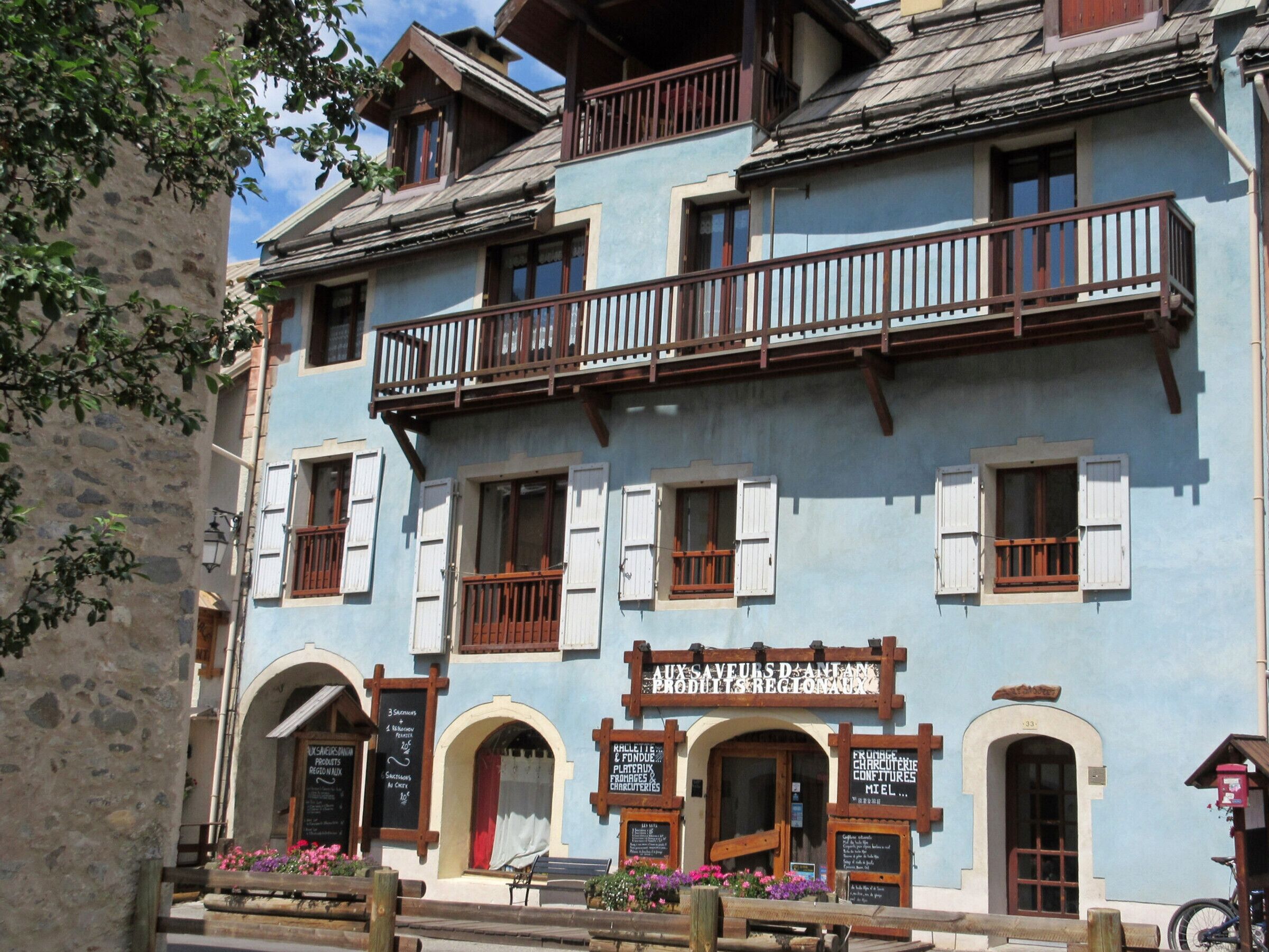 Ein traditionelles Gebäude mit Balkon, zahlreichen Fenstern und Schildern, die regionale Produkte und Dienstleistungen bewerben.