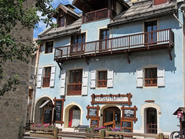 A traditional building with a balcony, multiple windows, and signs indicating local products and services.