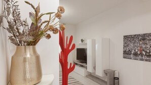Una sala de estar moderna con un jarrón beige de flores secas, una escultura abstracta roja, un televisor de pantalla plana y un cartel deportivo en blanco y negro en la pared.