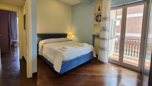 Ein Schlafzimmer mit einem Bett, einem Nachttisch, einem Fenster mit Vorhängen und Blick auf den Balkon.