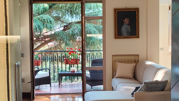 Ein Wohnzimmer mit einer Couch, einem Esstisch mit Stühlen, einem Balkon mit Blumentöpfen und einem Bild an der Wand.