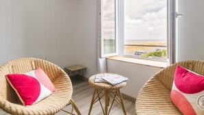 A balcony with wicker chairs, a small table, and a view of the beach. - Family house near the beach (Saint-Marcouf)
