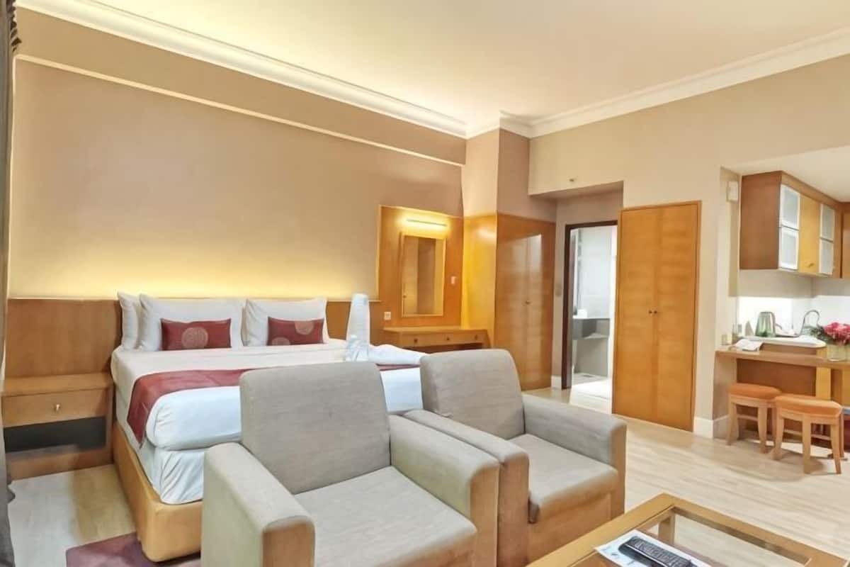 Une chambre d’hôtel comprenant un lit, deux fauteuils, un bureau, un miroir et une kitchenette.