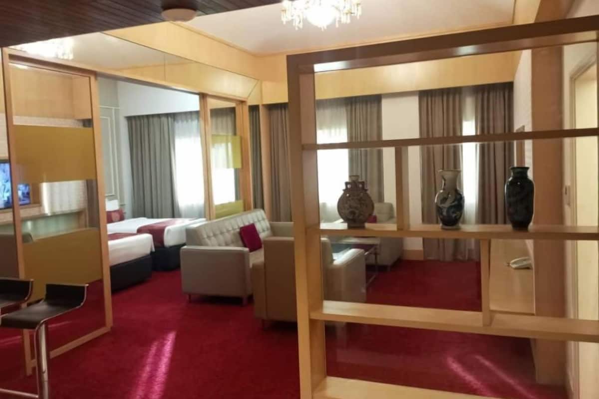 Une chambre d’hôtel avec un tapis rouge, un canapé, un lit, une télévision et un lustre.