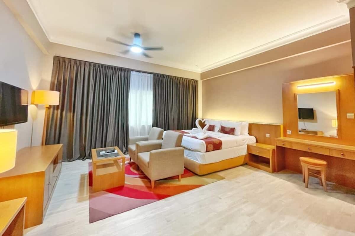 Une chambre d’hôtel équipée d’un lit, d’un bureau, d’une chaise, d’une télévision, d’un ventilateur de plafond et d’une grande fenêtre avec des rideaux.