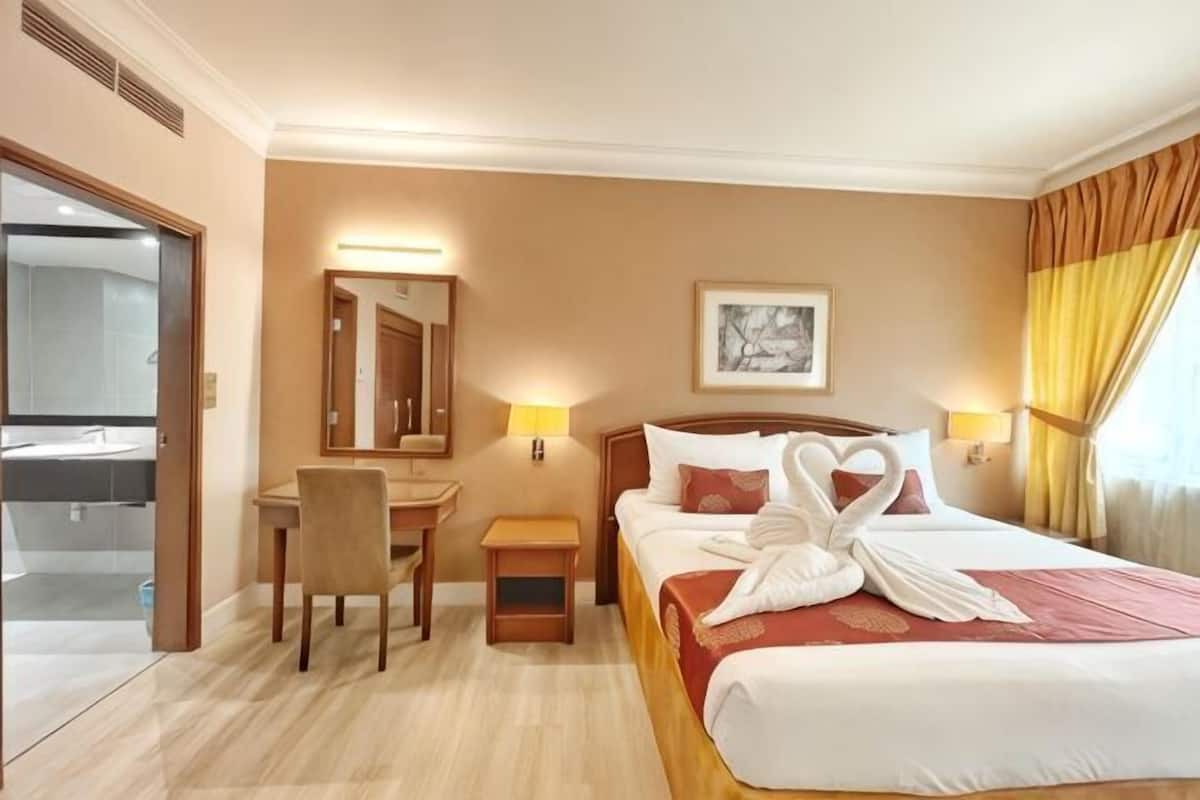 Une chambre d’hôtel avec un lit, un bureau, une chaise, une petite table, un miroir et un tableau au mur.