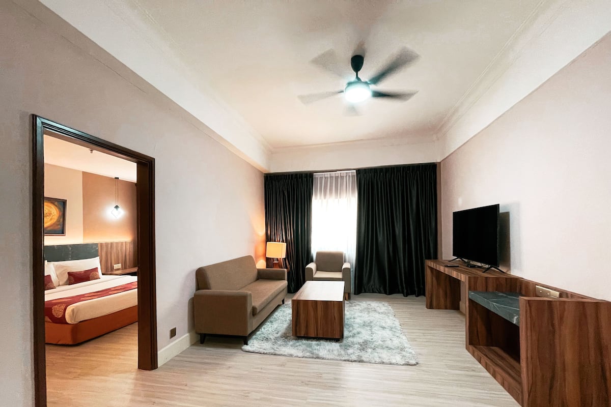 Une chambre d’hôtel comprenant un lit, un canapé, une télévision, une table d’appoint en bois et un ventilateur de plafond.