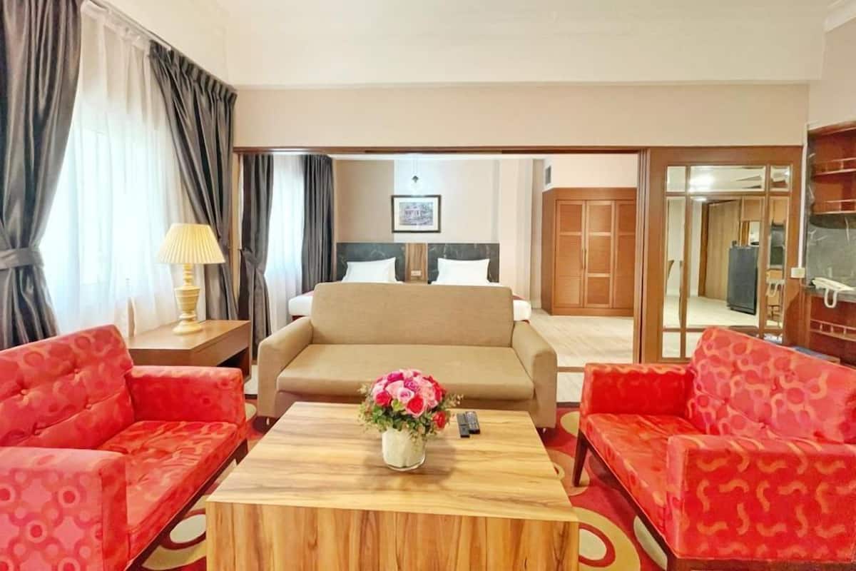 Une chambre d’hôtel avec un canapé, une table basse ornée d’un vase de fleurs, un lit avec une tête de lit et une armoire.