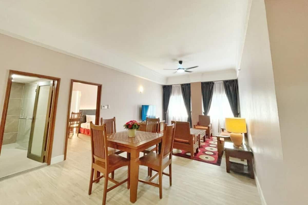 Une chambre d’hôtel comprenant un coin repas, un ventilateur de plafond, un canapé, une lampe et une vue sur l’extérieur par une fenêtre avec des rideaux.