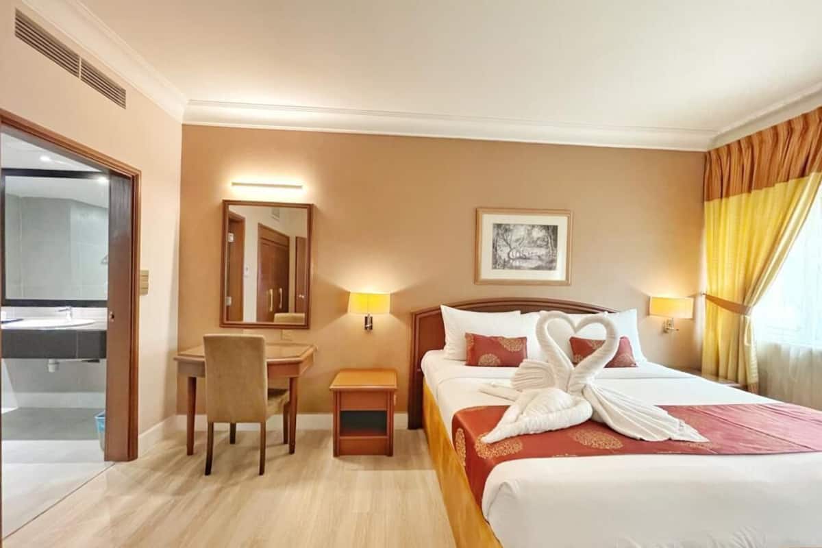 Une chambre d’hôtel comprenant un lit, un bureau, une chaise, une table de chevet, un miroir et un tableau encadré au mur.