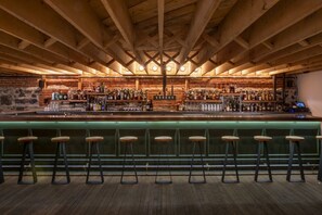 A bar with wooden beams, a brick wall, and a green bar counter with stools.