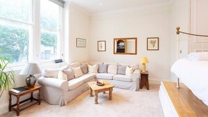A room with a large window, a sofa, a small table, a lamp, and a bed. - Charming Studio Apartment Near Clapham Common (London)