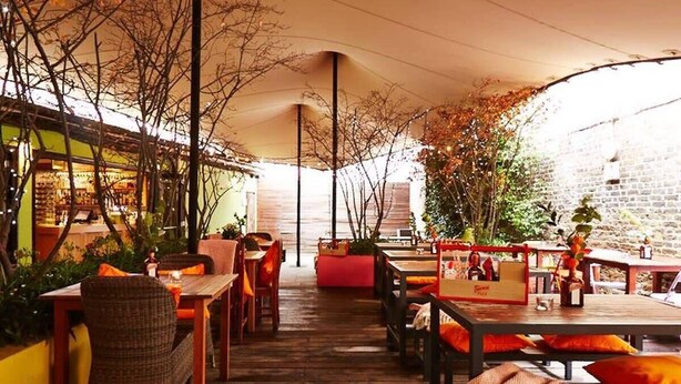 An outdoor dining area with wooden tables and chairs, covered by a canopy. - Charming Studio Apartment Near Clapham Common (London)