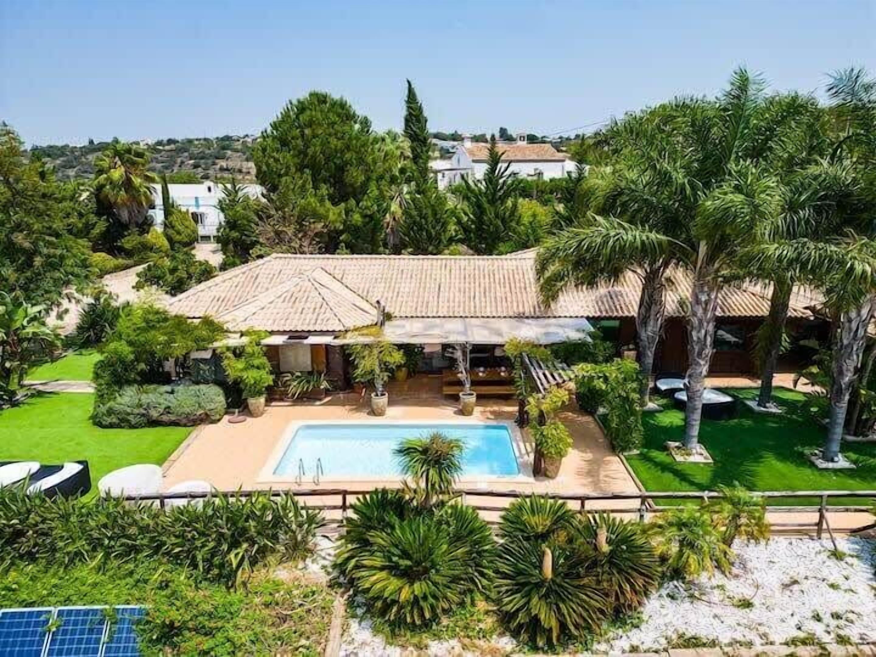 A villa with a swimming pool, surrounded by lush greenery and palm trees.