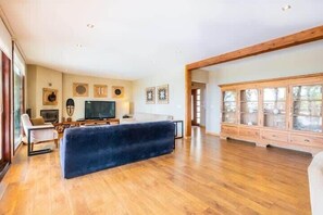 A spacious living room with a large dark sofa, wooden flooring, a television, and a cabinet with glass doors.