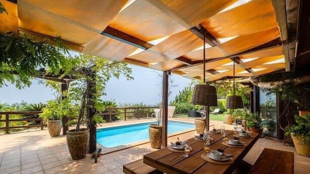 Ein Essbereich im Freien mit Pool, Holztischen und Kübelpflanzen.