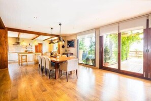 A spacious dining area with a wooden table and chairs, a kitchen in the background, and large sliding glass doors leading to an outdoor area.
