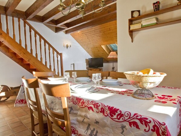 A dining area with a table set for four, a wooden staircase, and a television in the background.
