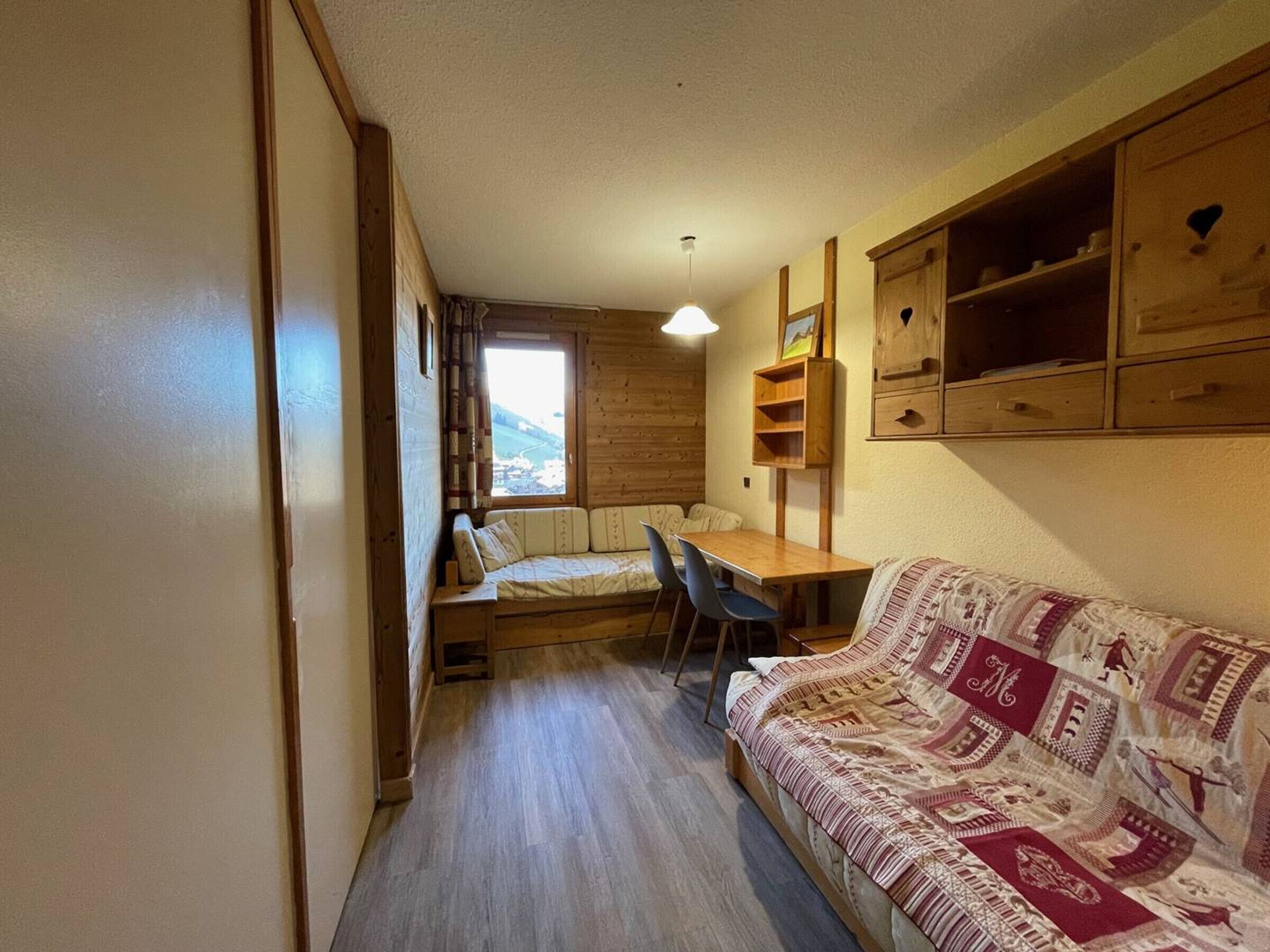 Une pièce de taille modeste, comprenant un lit superposé en bois, une petite table, un canapé et une fenêtre donnant sur un paysage.