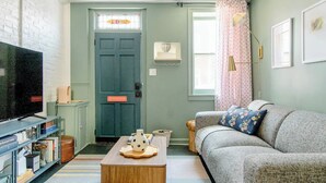 Ein gemütliches Wohnzimmer mit Fernseher, Bücherregal, Sofa und einer Tür mit Buntglasfenster.