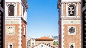 A view through a metal gate of a building with two towers, one with a clock and the other with a bell. - Eixample / Gran Vía Historic Catalan 4 bedrooms (Barcelona)