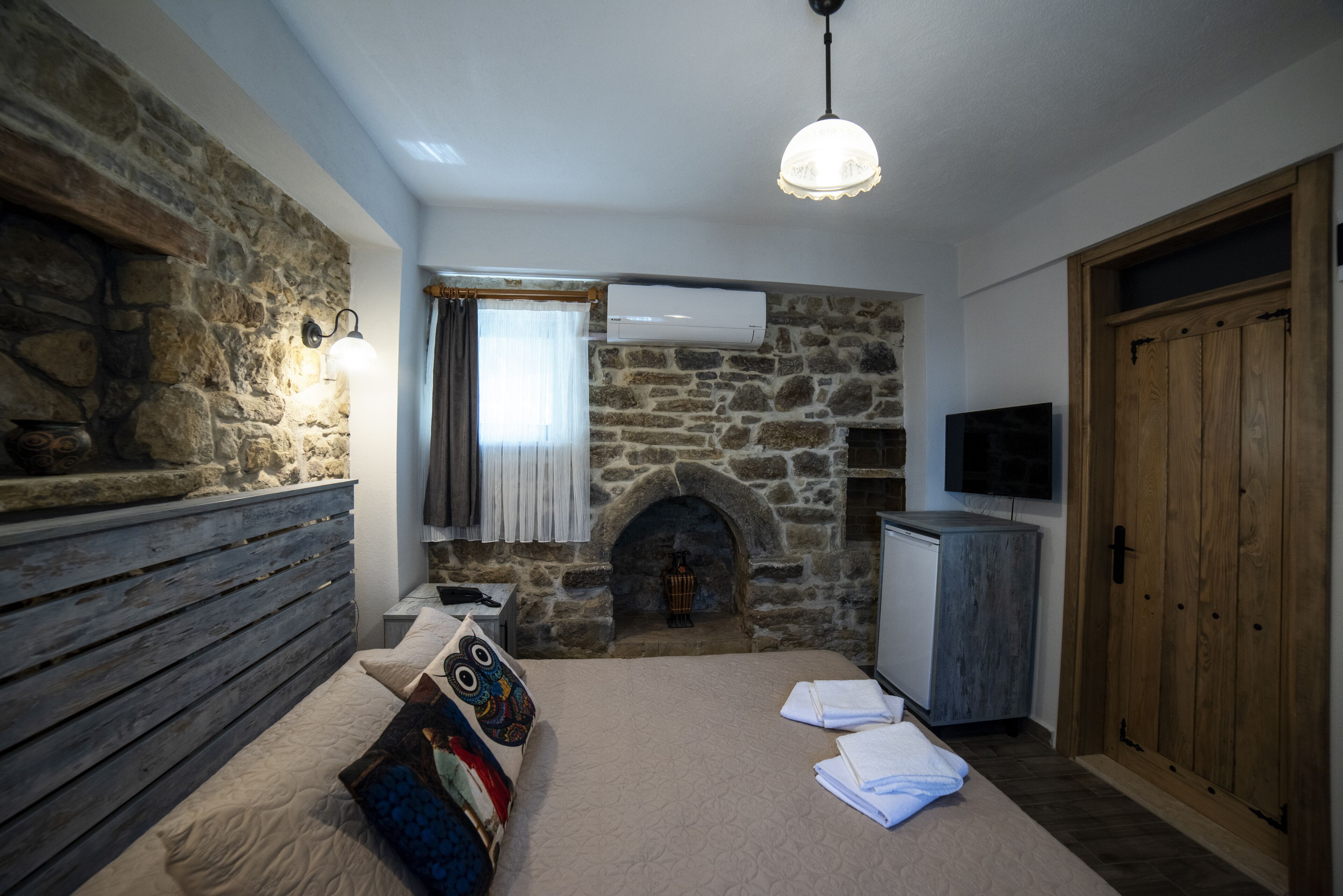 Ein Schlafzimmer mit Steinwand, Kamin, einem Bett mit Zierkissen, einem Nachttisch und einem Fernseher.