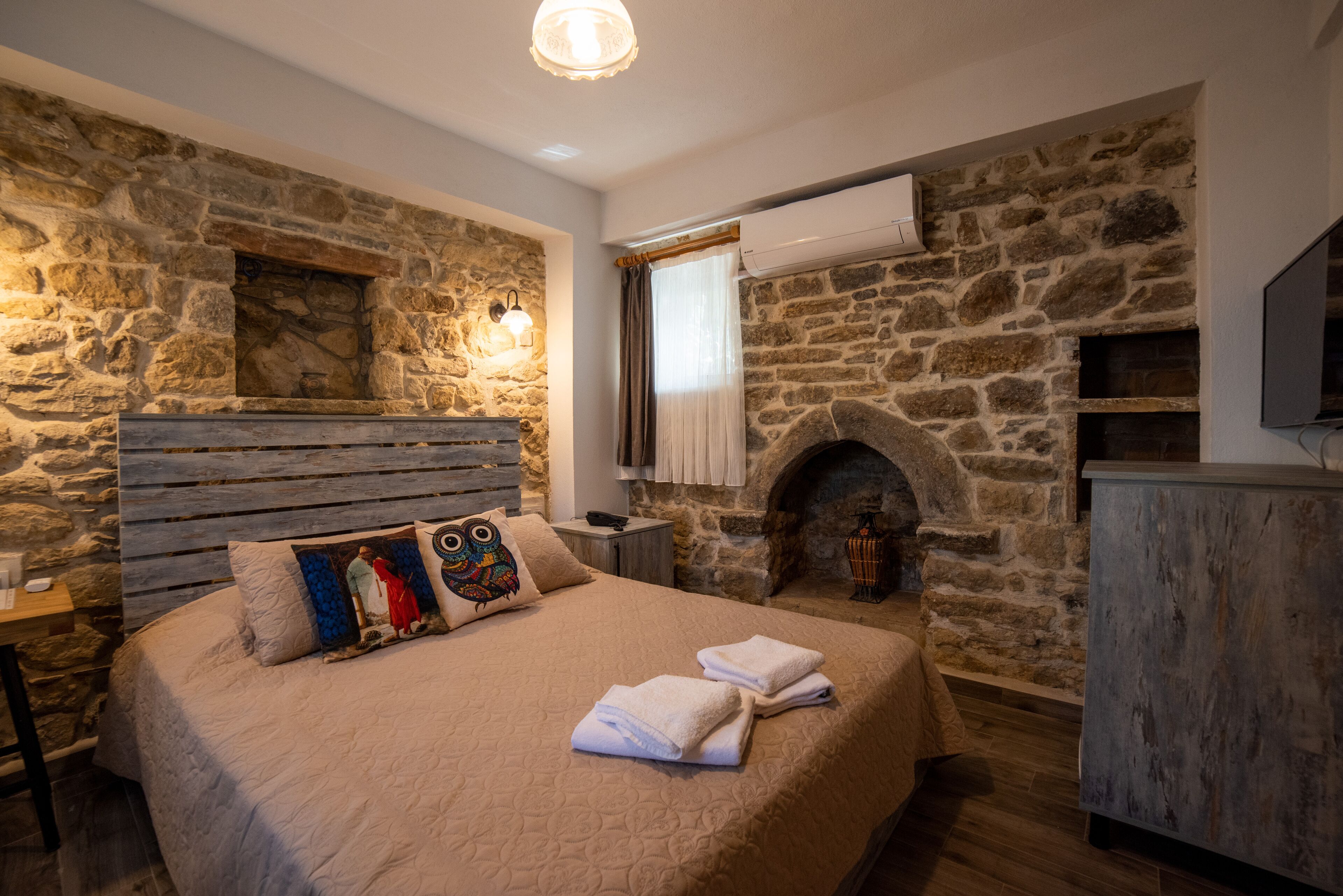 A bedroom with a stone wall, a fireplace, a bed with towels, and a nightstand.