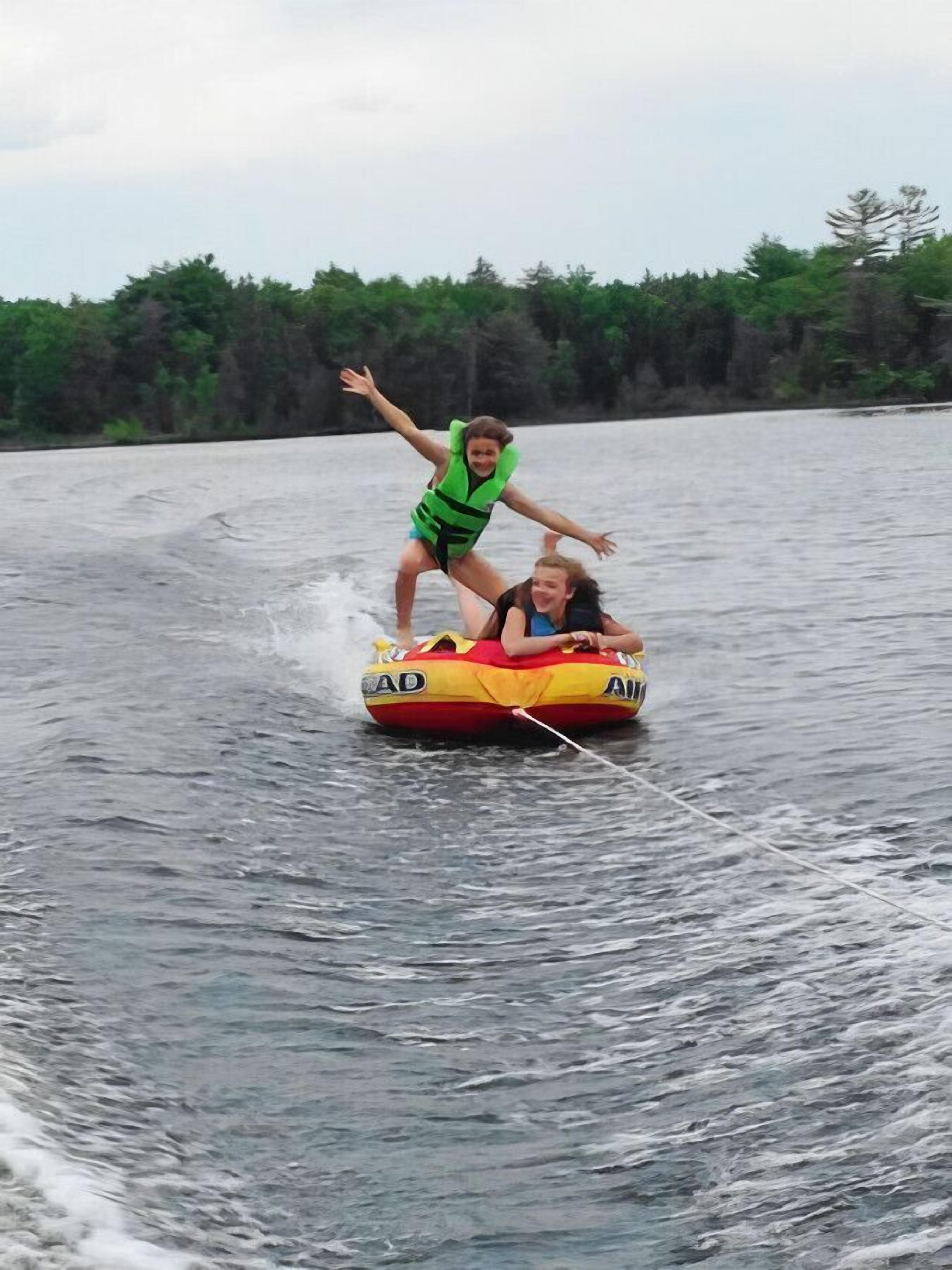 Two people on a watercraft with 'AD' branding, surrounded by water and trees.