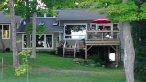 Una casa con un porche, un espacio cubierto con un paraguas rojo y una canoa en el jardín.