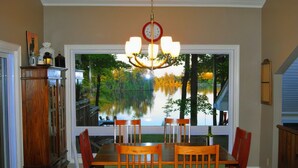 Comedor con amplia ventana con vistas a un lago, candelabro y mobiliario de madera.