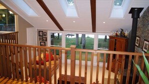 Amplia sala de estar con escalera de madera, un ventanal con vistas al exterior y una chimenea.