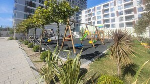 A playground with swings and slides, surrounded by a building with multiple balconies. - Cozy Retreat: Stylish 1BR Apt (Esenyurt)