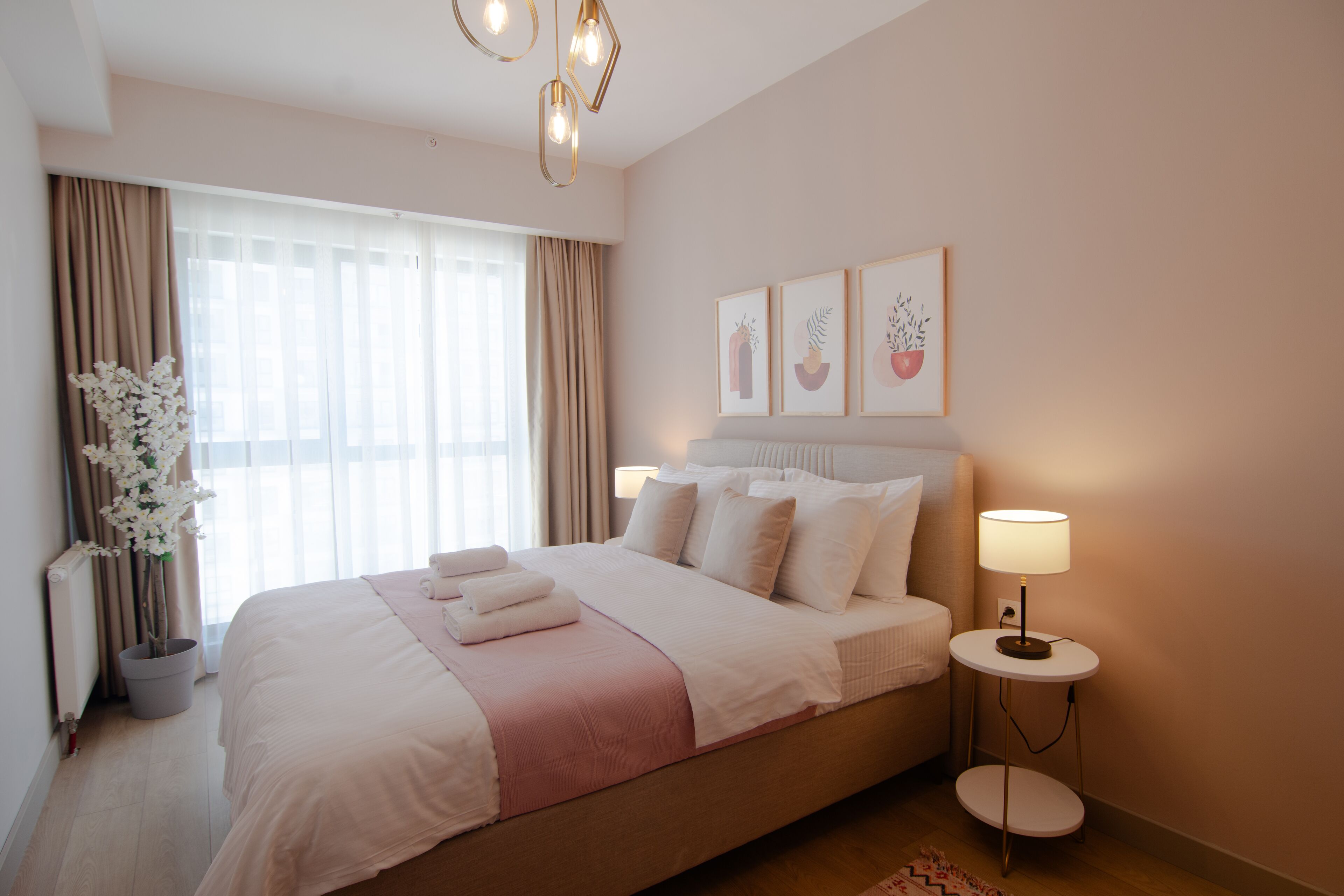 Een hotelkamer met een groot bed, bedlampen, een potplant en kunst aan de muur.
