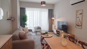 A modern living room with a sofa, a dining table, a TV, and a large window with curtains. - Cozy Retreat: Stylish 1BR Apt (Esenyurt)