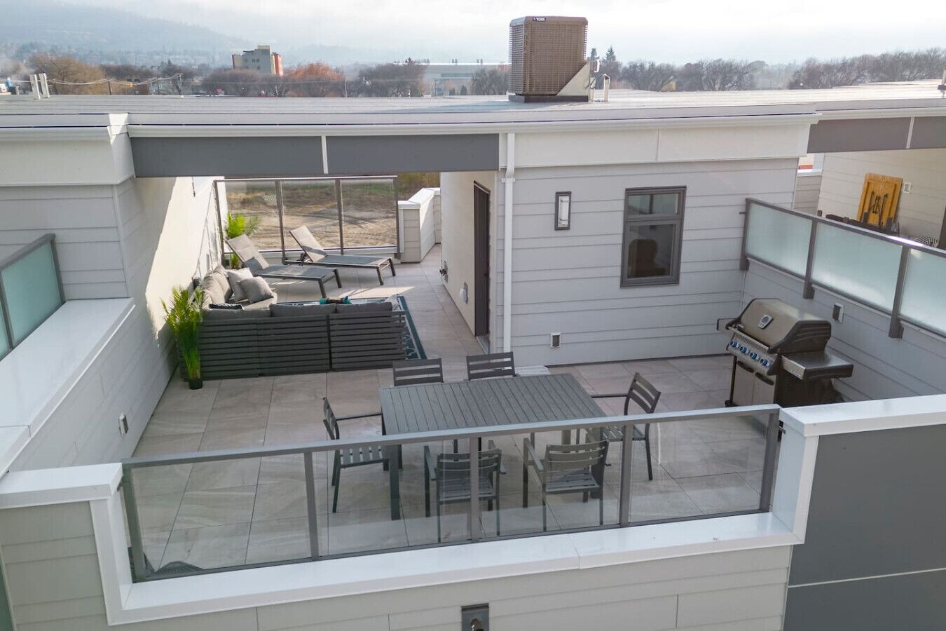 Une terrasse sur le toit avec une table, des chaises, un barbecue et un petit coin salon.