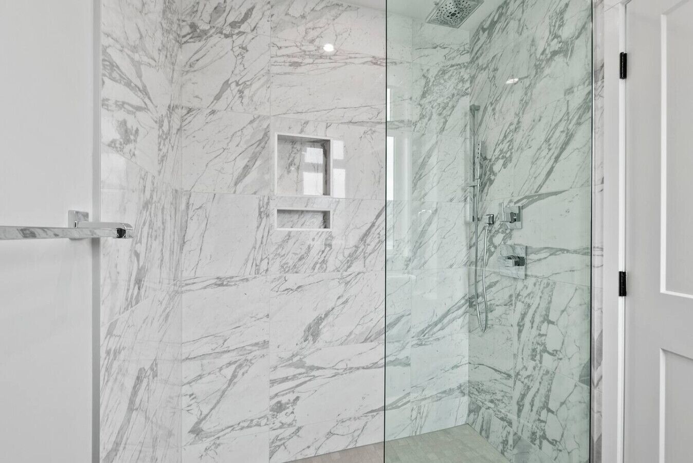 A modern bathroom with a glass-enclosed shower, marble walls, and a small window.