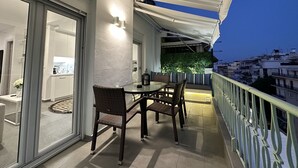A balcony with a glass door leading to a kitchen, wicker furniture, and a green wall. - Lusso Bianco Nilie Hospitality MGMT (Thessaloniki)