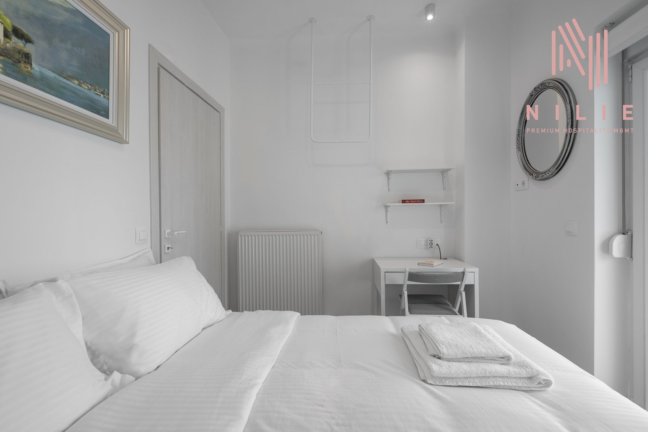 A hotel room with a bed, a desk, a chair, a radiator, and a framed picture on the wall.