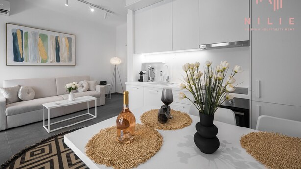 A modern, minimalist living room with a white sofa, a coffee table, and a painting on the wall. - Lusso Bianco Nilie Hospitality MGMT (Thessaloniki)