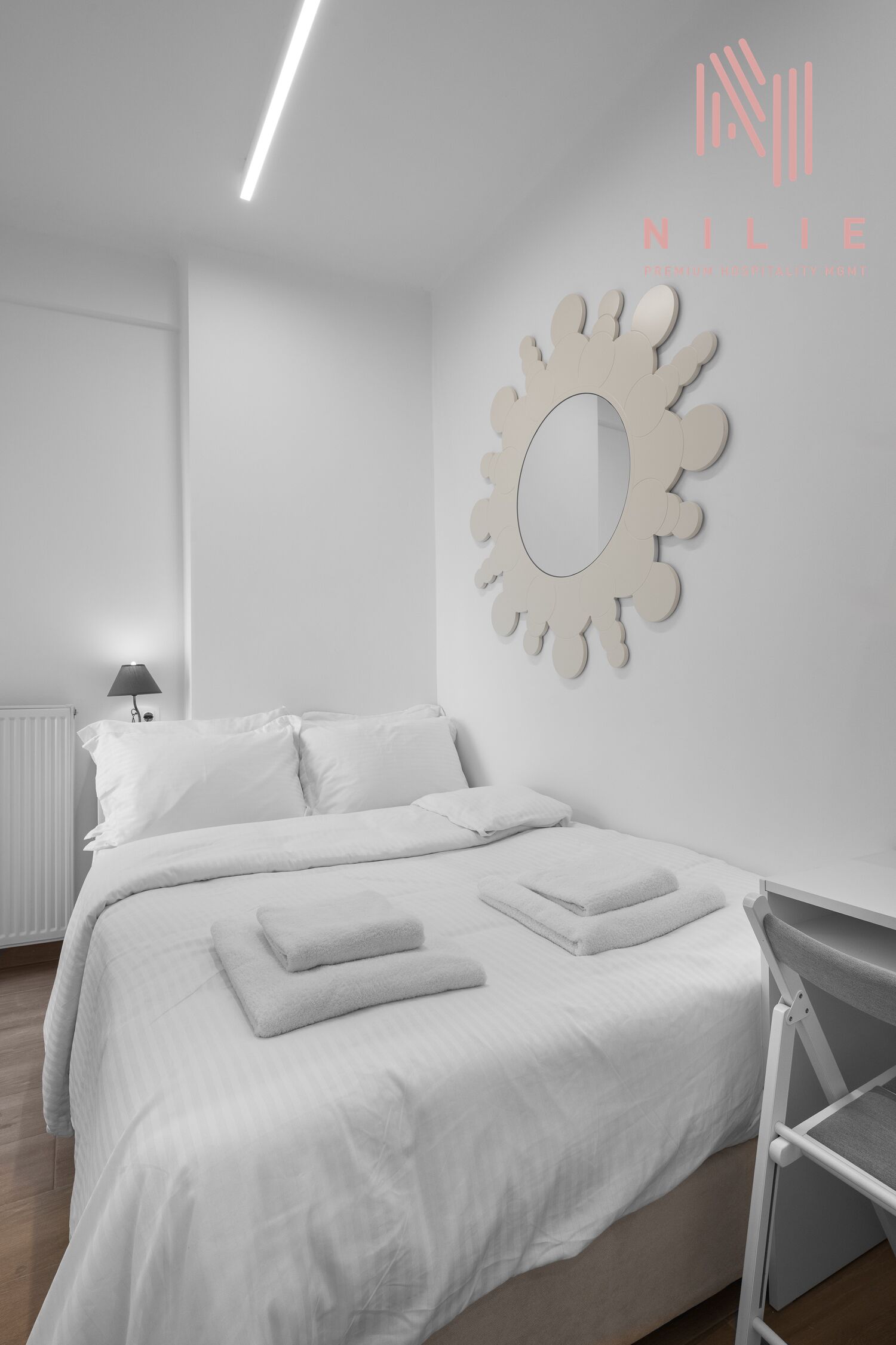 A modern, minimalist bedroom with a neatly made bed, a unique wall mirror, and a radiator.