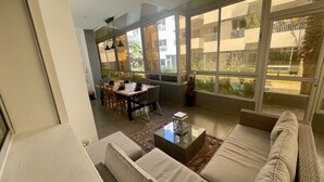 Un salon moderne avec un canapé, une table à manger et des chaises, ainsi que de grandes fenêtres donnant sur l’extérieur.