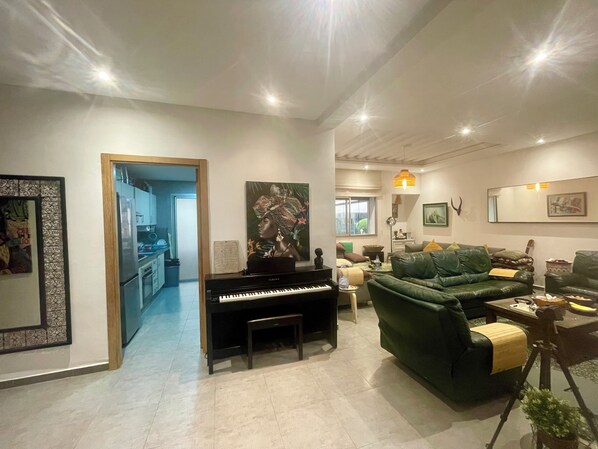 A living room with a piano, green sofa, and a dining area with a table and chairs.