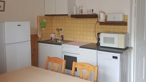 Una cocina compacta con refrigerador, estufa, microondas y pileta. Hay dos sillas de madera y una mesa.