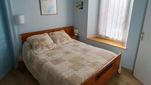 Un dormitorio con cama, ventana, mesita de noche y lámpara fijada a la pared.