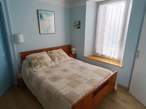 Une chambre à coucher avec un lit, une fenêtre, une table de chevet et une lampe fixée au mur.