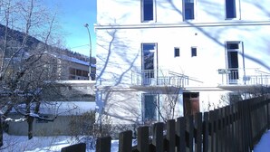 Un edificio de varios pisos con un balcón, una valla de madera en primer plano y suelo cubierto de nieve.