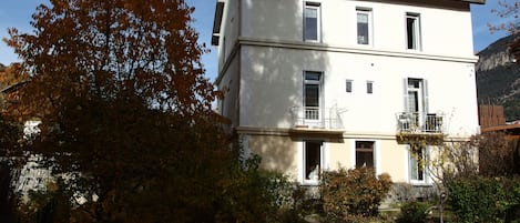Un bâtiment à deux étages doté d’un balcon au deuxième étage, entouré d’arbres et bordé d’un sentier.