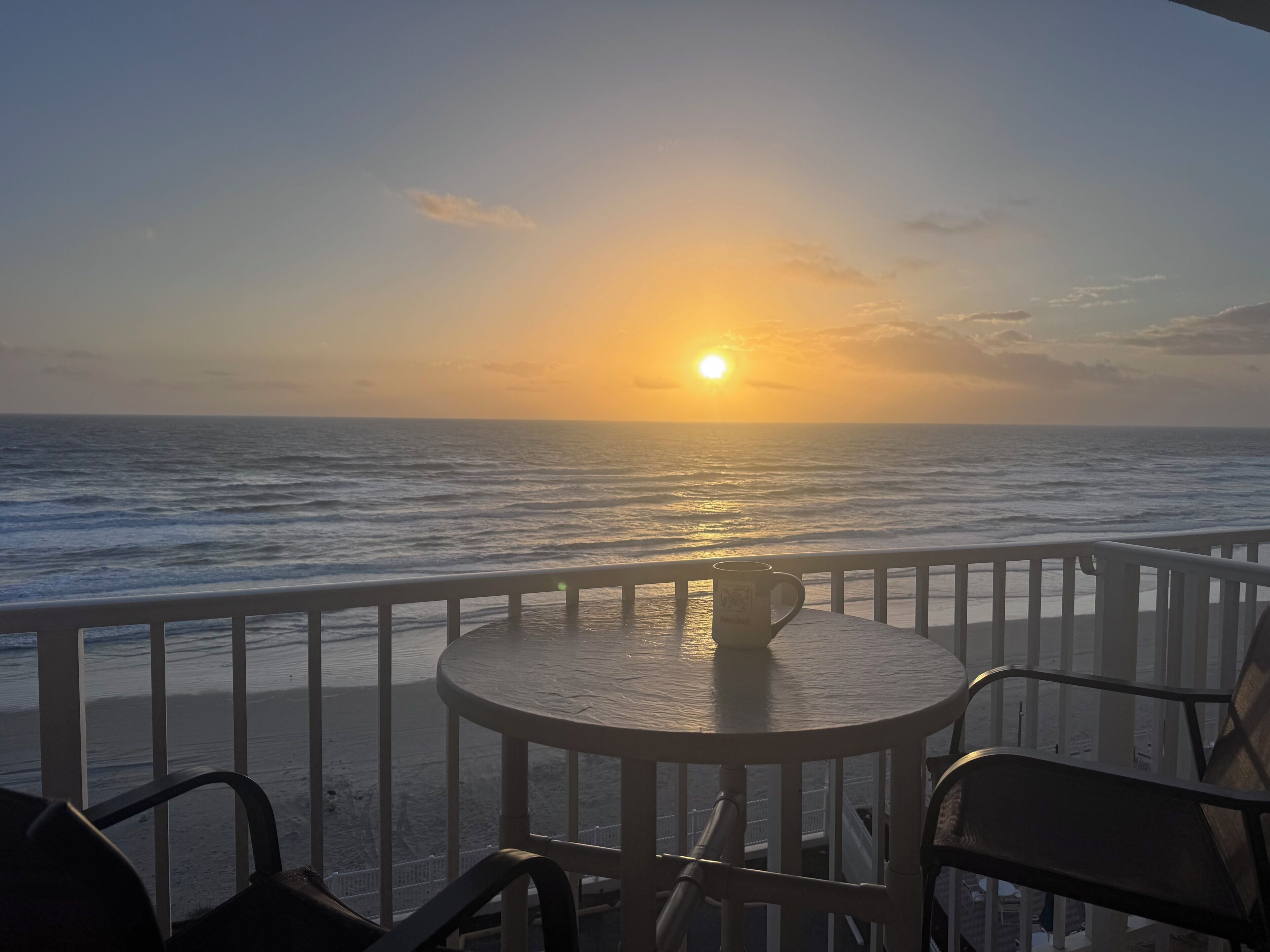 Uitzicht op zee, met een tafel en stoelen, een hekwerk en een mok op tafel.