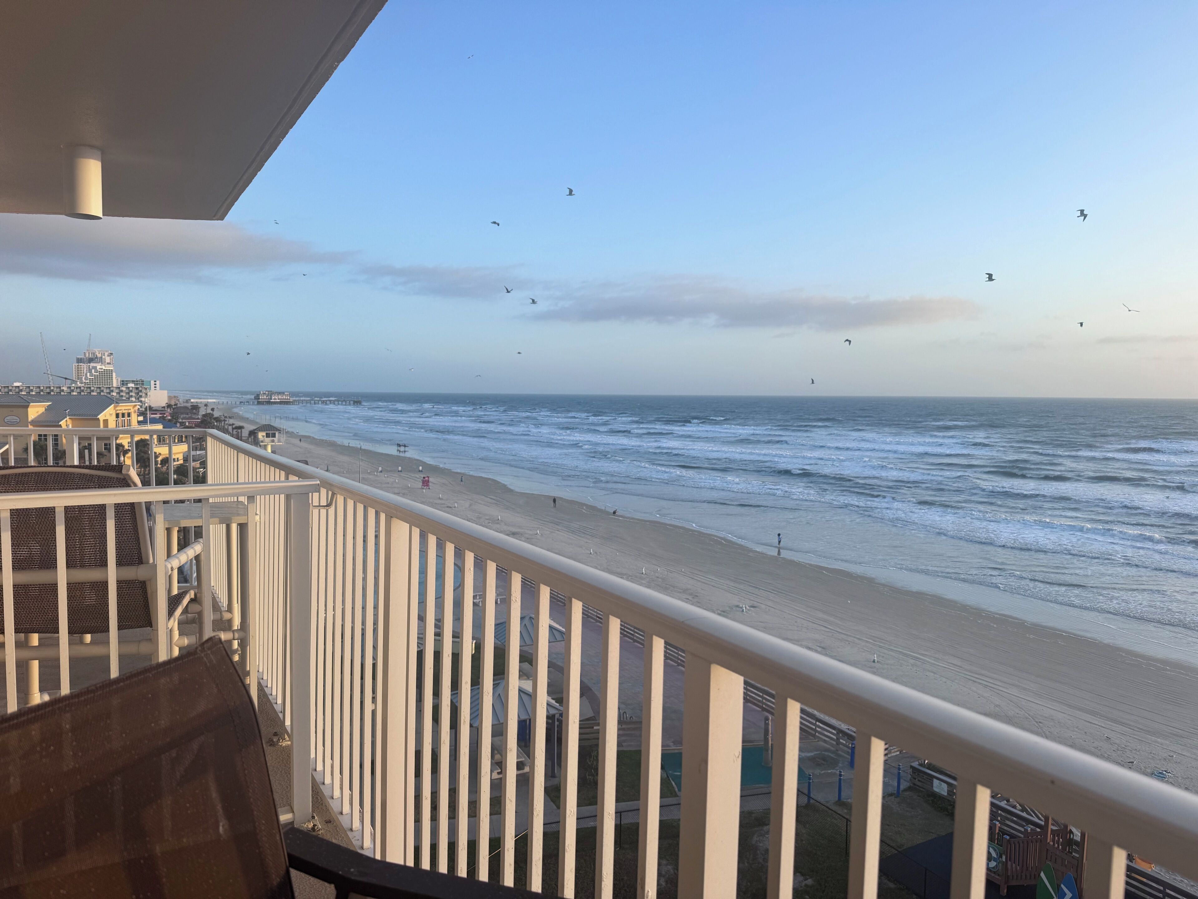 Een balkon met uitzicht op het strand en de oceaan, een hekwerk en een glimp van de skyline op de achtergrond.
