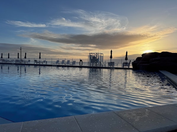 Ein Swimmingpool mit Sonnenuntergangsblick, einem Zaun und Liegestühlen.
